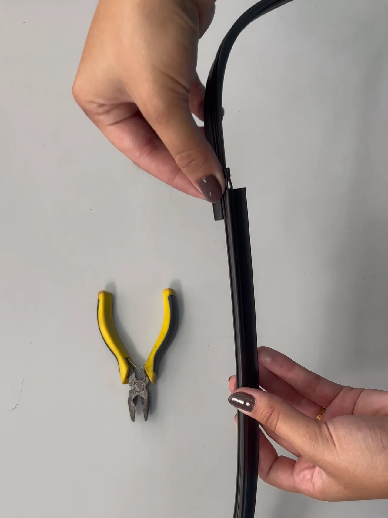 Uma pessoa coloca um refil de borracha novo na estrutura de uma palheta, ao lado de um alicate.
